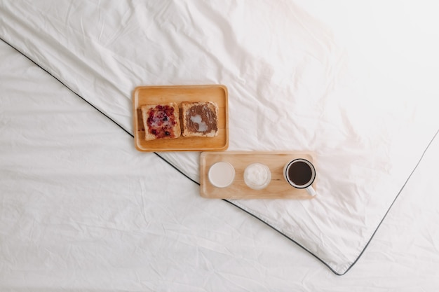 Juego de desayuno de pan y mermelada con leche y café en la cama blanca