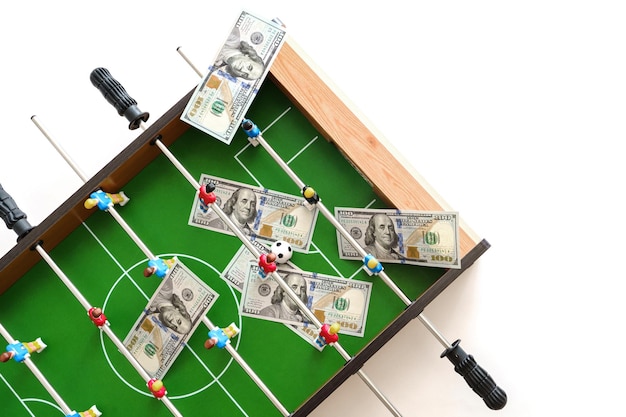 Juego de futbolín con billetes de dólares estadounidenses esparcidos a su alrededor aludiendo a un concepto de apuestas