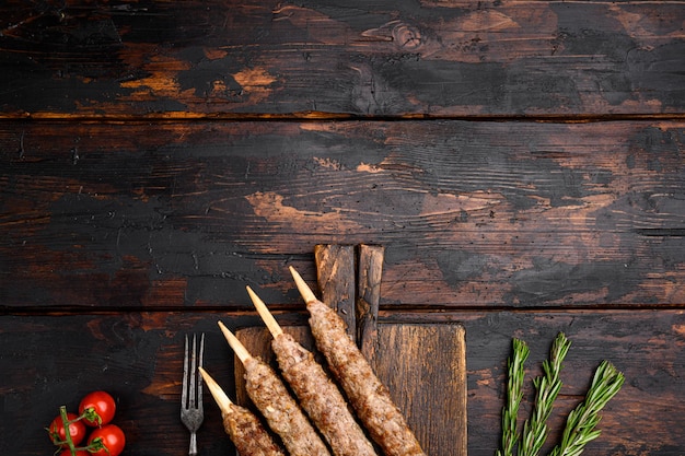 Juego de kebabs tikka, shish y kofta, en una tabla para servir, sobre un fondo de mesa de madera oscura antigua, vista superior plana, con espacio para copiar texto