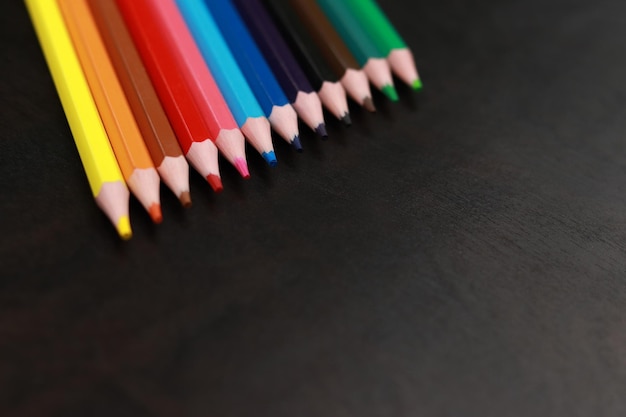 Un juego de lápices de colores sobre un fondo de madera negra. Lápices brillantes afilados