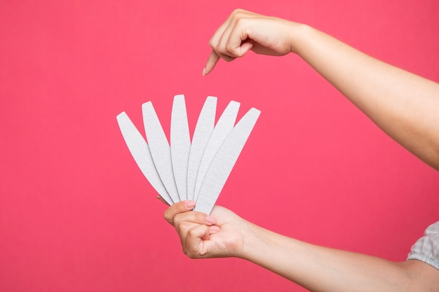 Juego de limas de uñas en mano de mujer y apunta a uno de ellos sobre fondo rosa. equipo de manicurista