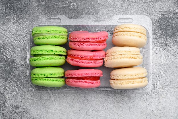 Juego de macarons de colores dulces, en paquete de plástico, sobre fondo de mesa de piedra gris, vista superior plana