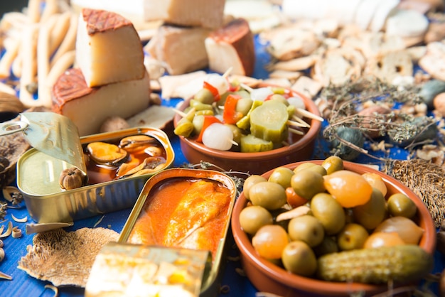 Juego de mesa con un aperitivo compuesto por diferentes alimentos, quesos y latas de encurtidos.