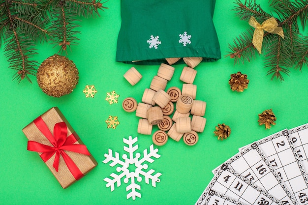 Foto juego de mesa de lotería. barriles de madera de lotería con bolsa y tarjetas de juego para un juego de lotería, ramas de abeto de navidad, conos, pelota de juguete, snowflackes y caja de regalo sobre fondo verde. vista superior