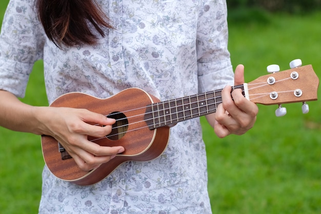 Juego de mujer joven en la guitarra de ukelele marrón en el jardín