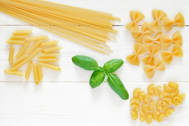 Juego de pasta de espagueti farfalle crudo maccheroni albahaca de hoja verde sobre fondo de tablero de madera blanca espacio de vista superior para copiar texto