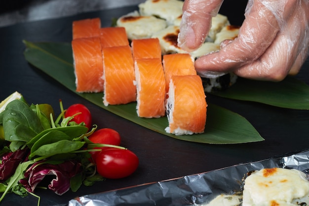 juego de rollos de sushi se encuentra en hojas de bambú con limón, hierbas y tomates rojos, servido en una pizarra de piedra negra.