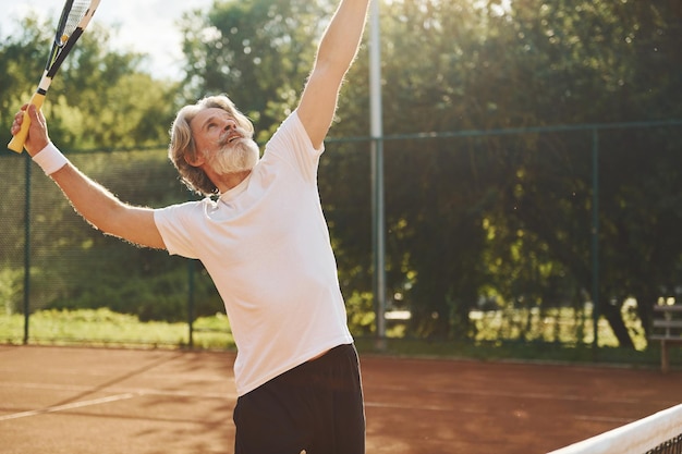Juego Senior hombre moderno y elegante con raqueta al aire libre en la cancha de tenis durante el día