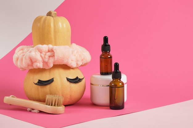 Juego simulado de envases cosméticos y calabaza con diadema y pestañas postizas sobre fondo rosa