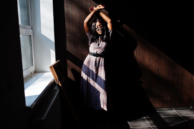 Juego con sombras Retrato de moda de mujer afroamericana en vestido largo y anteojos interior