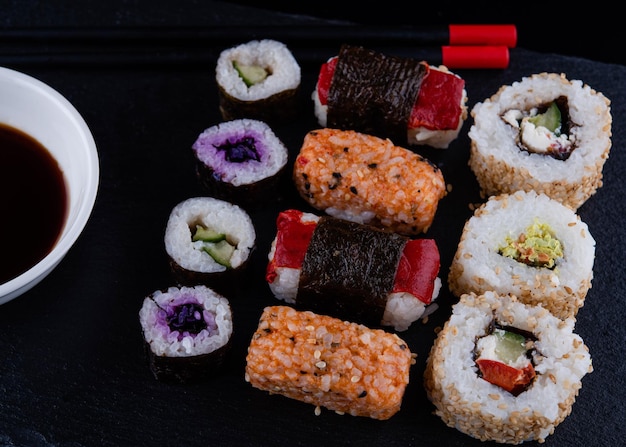 Juego de sushi con palillos y soja en un plato negro listo para comer sobre fondo negro