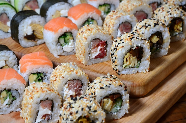 El juego de sushi de varios rollos se encuentra en una tabla de cortar de madera sobre una mesa en la cocina de una barra de sushi