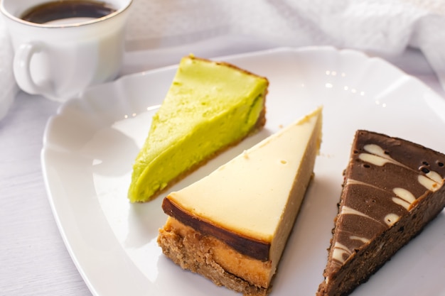 Juego de tarta de queso de Nueva York, chocolate y pistacho en plato blanco y taza de café. De cerca.