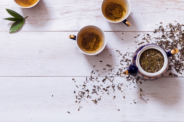 Juego de té tazas, tetera y té preparado con hojas secas en la mesa de madera blanca