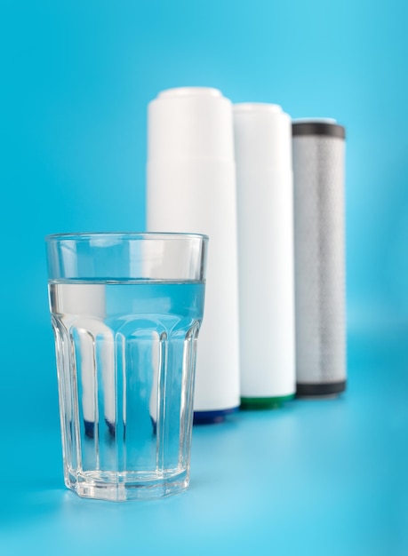 Juego de tres cartuchos para filtro de agua con un vaso de agua transparente sobre fondo azul Agua conceptual