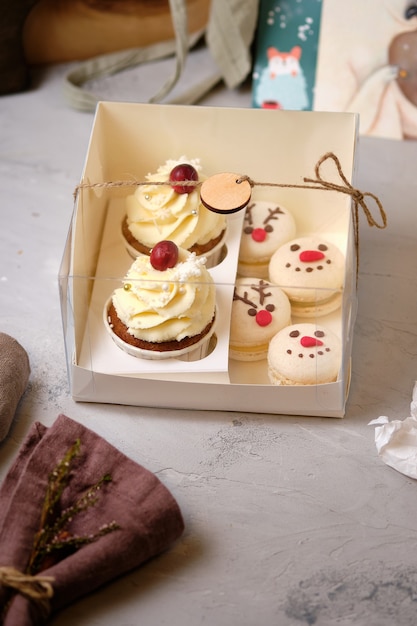 Juegos de dulces de regalo de año nuevo. Una caja de cupcakes y macarons como regalo de Navidad. Cupcakes con crema de queso crema y relleno de caramelo de maní y tartas de macarons con relleno de mandarina.