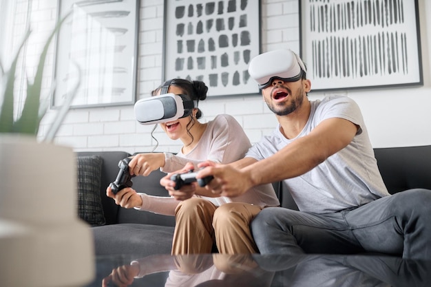 Juegos de realidad virtual y metaverso con una pareja jugando videojuegos en su casa juntos para divertirse o disfrutar del juego de realidad virtual y 3d ai con un hombre y una mujer que se unen en la sala de estar de una casa