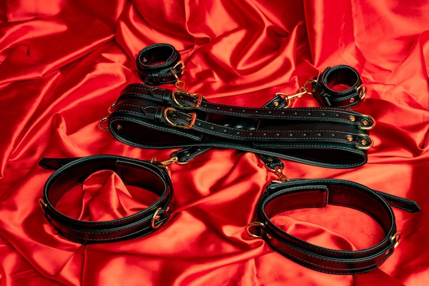 Juegos sexuales para adultos Artículos BDSM Correas de cuero esposas y bola de mordaza en una sábana de satén rojo