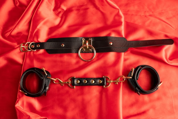 Juegos sexuales para adultos. Artículos BDSM. Esposas de correas de cuero, cuello sobre una sábana de raso rojo.