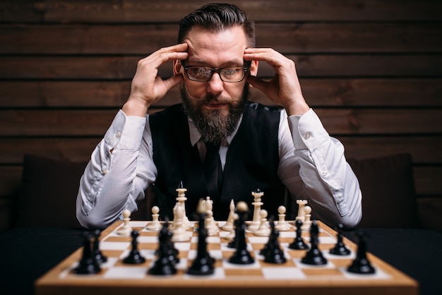 Jugador de ajedrez masculino pensativo en vasos pensando en la estrategia del juego.