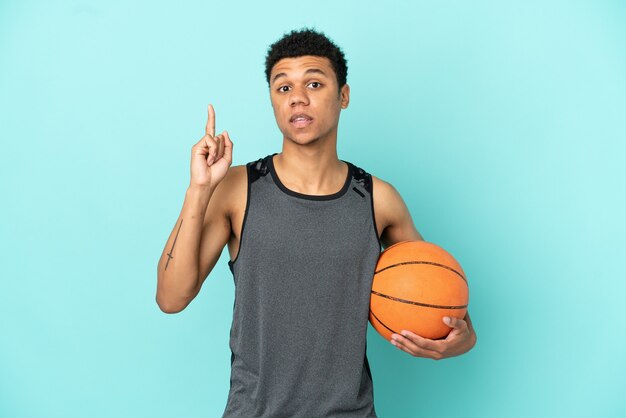 Jugador de baloncesto afroamericano aislado sobre fondo azul pensando en una idea apuntando con el dedo hacia arriba