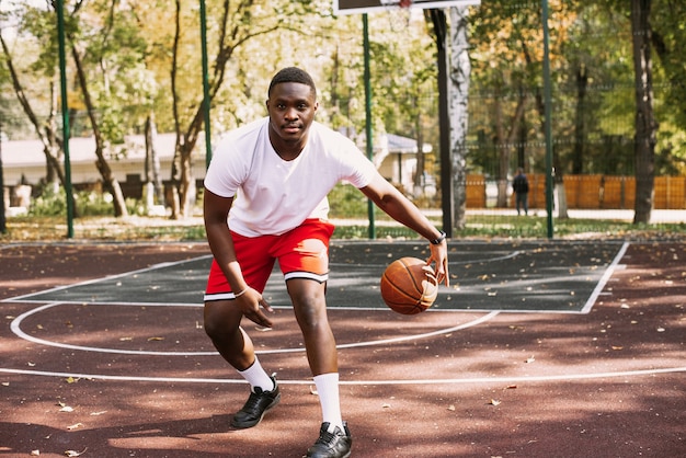 Jugador de baloncesto afroamericano en un campo de deportes al aire libre jugando con una pelota. haciendo deporte en la calle.