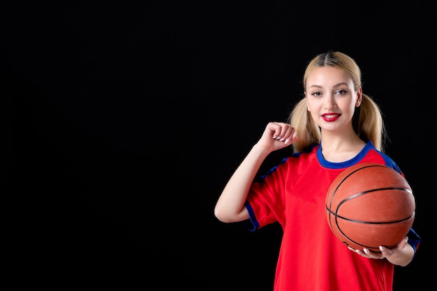 Jugador de baloncesto femenino con balón sonriendo sobre fondo negro juego de atleta