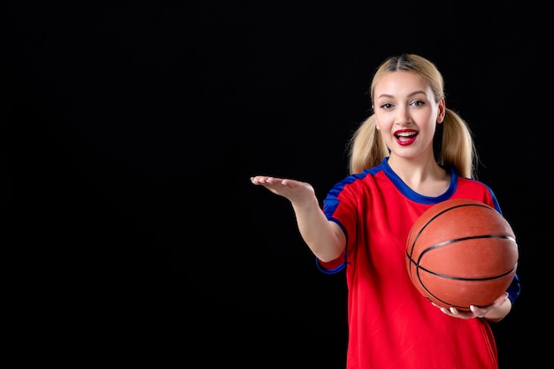 Jugador de baloncesto femenino con bola apuntando a algo sobre fondo negro atleta del juego