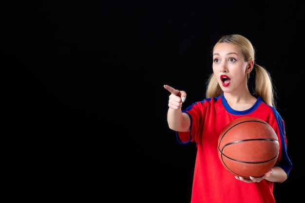 Jugador de baloncesto femenino con bola apuntando a algo sobre fondo negro juego atleta