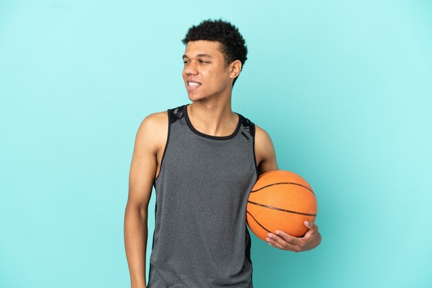 Jugador de baloncesto hombre afroamericano aislado sobre fondo azul mirando hacia el lado y sonriendo