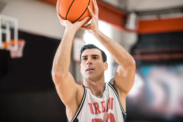 Jugador de baloncesto. Hombre joven con tatoo lanzando una pelota en un anillo