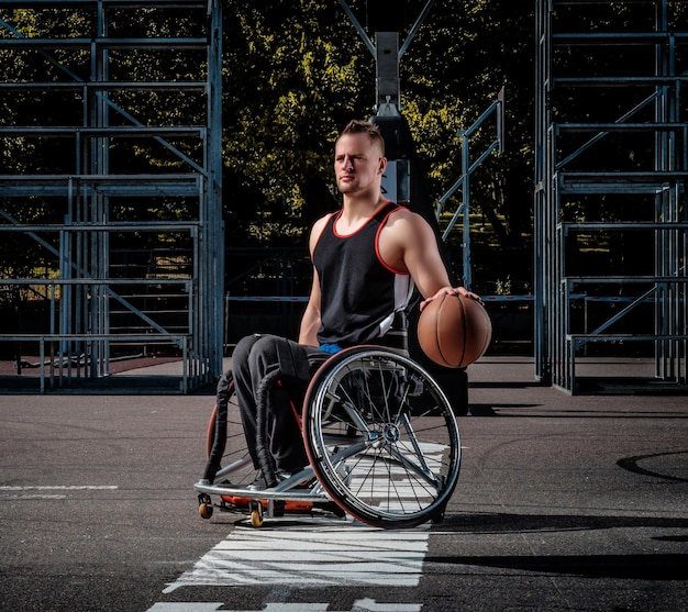 Un jugador de baloncesto lisiado en silla de ruedas sostiene una pelota en un campo de juego abierto.