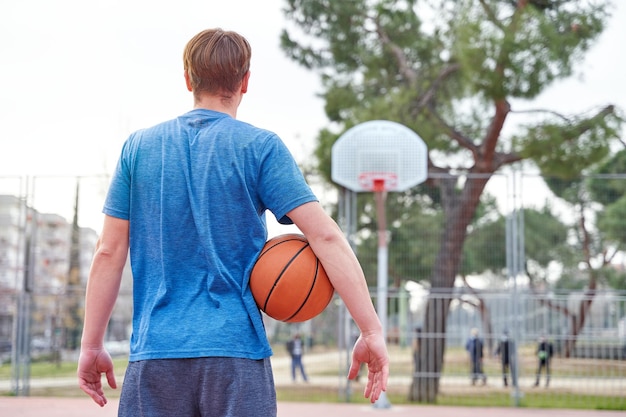 Jugador de baloncesto mirando la canasta antes de lanzar al joven con la pelota y ropa deportiva