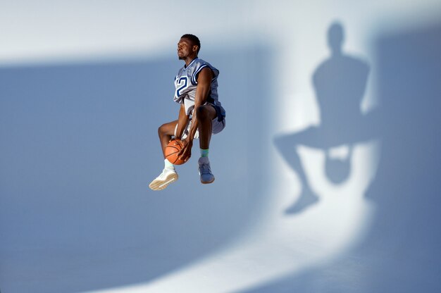 Foto el jugador de baloncesto con pelota muestra su habilidad, salto de altura en acción. baller profesional masculino en ropa deportiva jugando al deporte, deportista alto