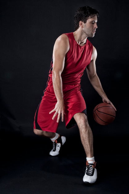 Jugador de baloncesto con una pelota en sus manos y un uniforme rojo. estudio fotografico.