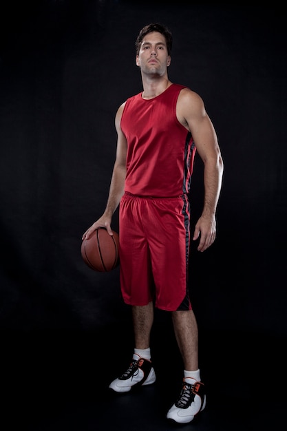 Jugador de baloncesto con una pelota en sus manos y un uniforme rojo. estudio fotografico.
