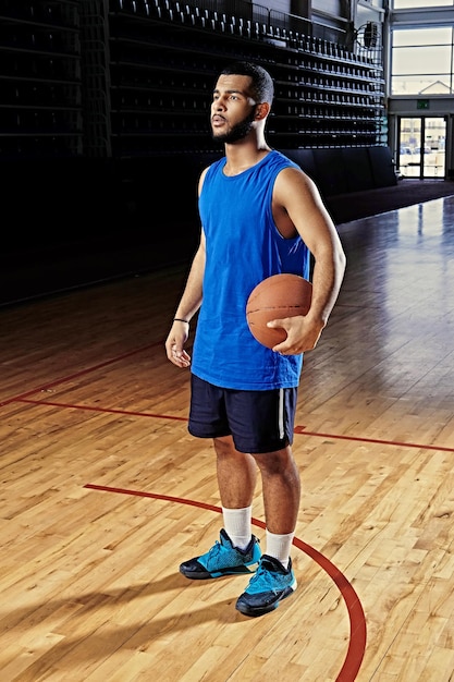 El jugador de baloncesto profesional negro sostiene una pelota sobre el aro en una sala de juegos.