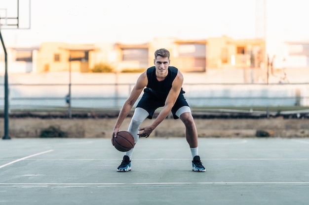 Jugador de baloncesto rebotando la pelota mientras mira a la cámara en una cancha al aire libre