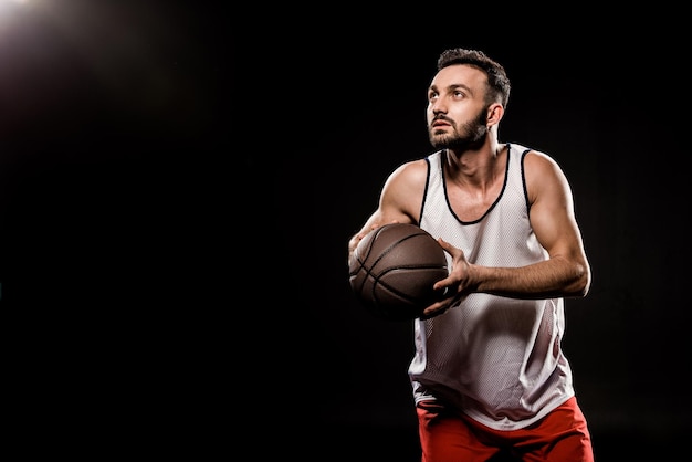 jugador de baloncesto serio sosteniendo la pelota en fondo negro