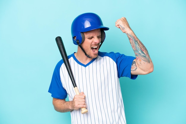 Jugador de béisbol con casco y bate aislado de fondo azul celebrando una victoria