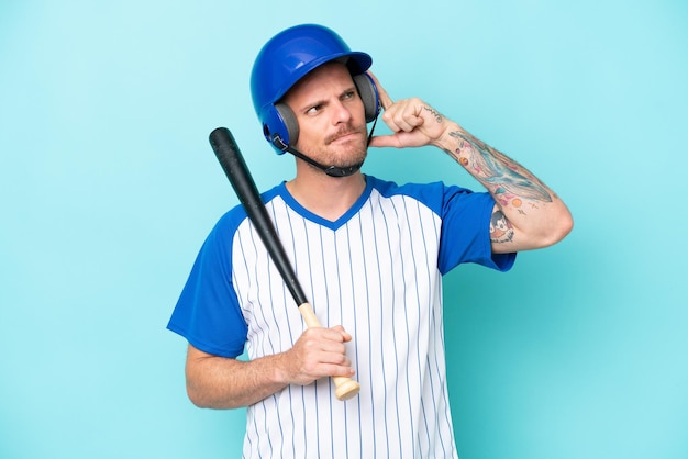 Jugador de béisbol con casco y bate aislado de fondo azul con dudas y pensando