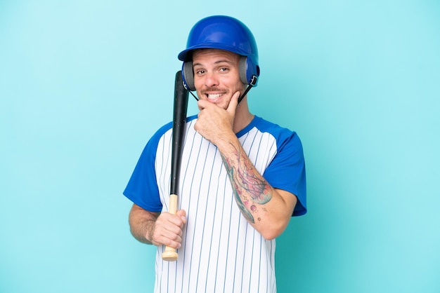 Jugador de béisbol con casco y bate aislado sobre fondo azul feliz y sonriente