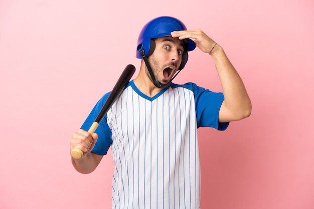 Jugador de béisbol con casco y bate aislado sobre fondo rosa haciendo gesto de sorpresa mientras mira hacia el lado