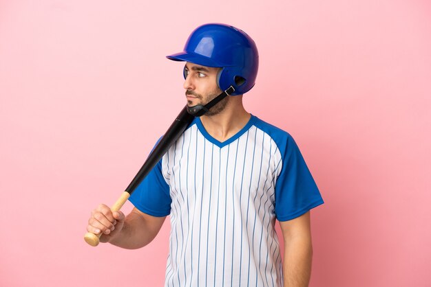 Jugador de béisbol con casco y bate aislado sobre fondo rosa mirando hacia el lado