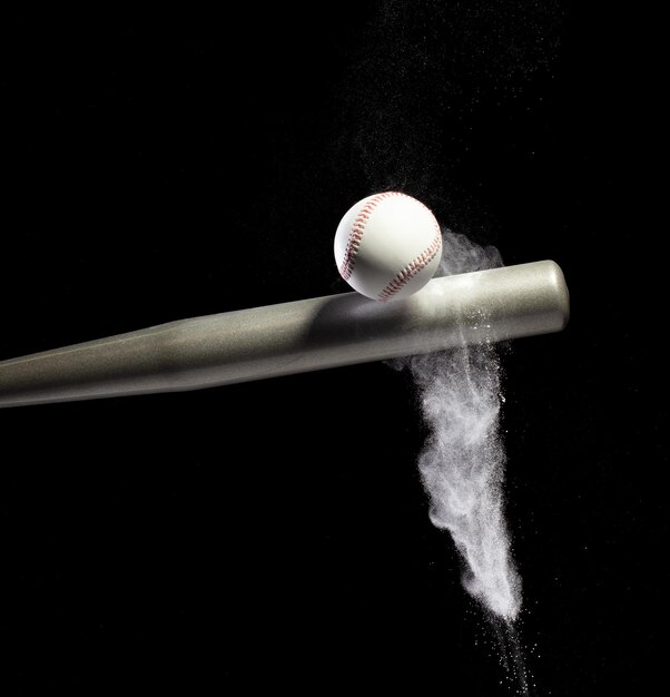 El jugador de béisbol golpea la pelota con un bate de plata y el suelo de arena explota en el aire Los jugadores de béisbal en acción dinámica golpean la pelota humo cola fondo negro acción de congelación aislada