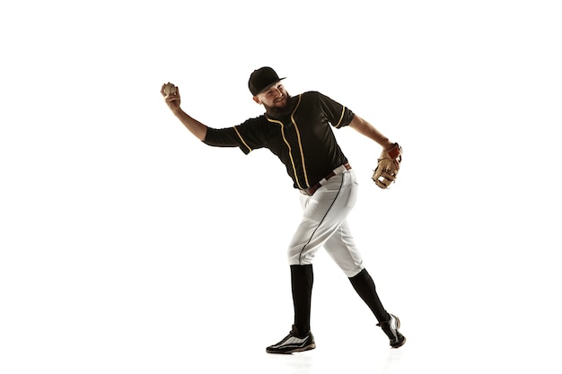 Jugador de béisbol, lanzador con uniforme negro practicando y entrenando aislado en una pared blanca. Joven deportista profesional en acción y movimiento. Estilo de vida saludable, deporte, concepto de movimiento.