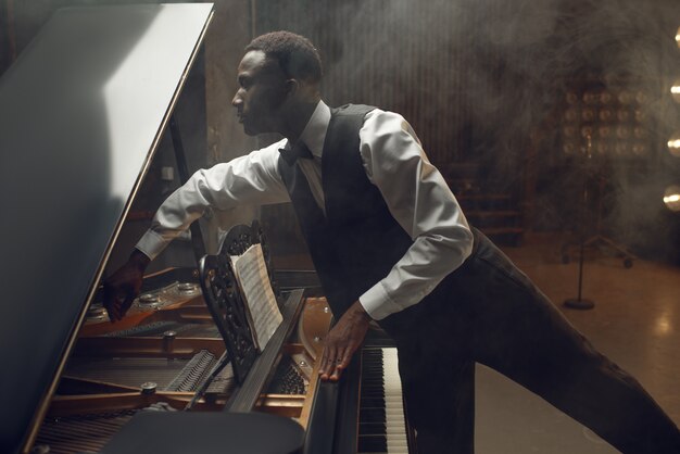 Jugador de ébano que afina el piano de cola en el escenario con focos. artista posa en instrumento musical antes del concierto