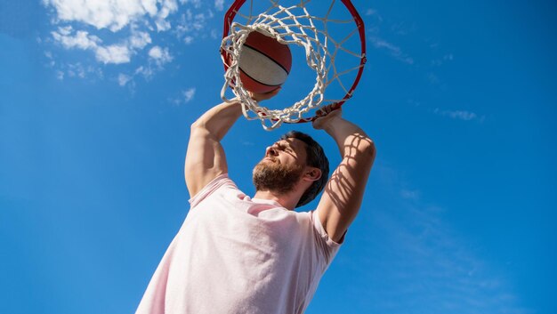 Un jugador exitoso lanza una pelota de baloncesto a través de la canasta en el verano de fondo del cielo