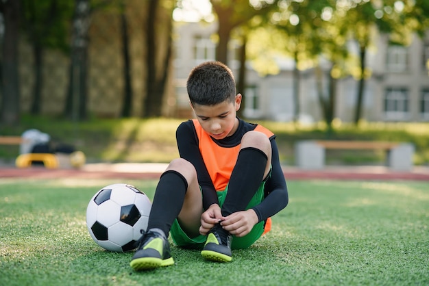 Jugador de fútbol adolescente en el campo de deportes al aire libre atando los cordones de las botas.