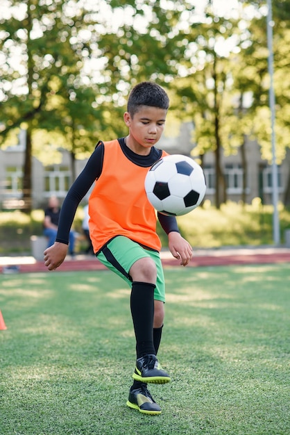 Foto el jugador de fútbol adolescente hábil concentrado rellena el balón de fútbol en la pierna.